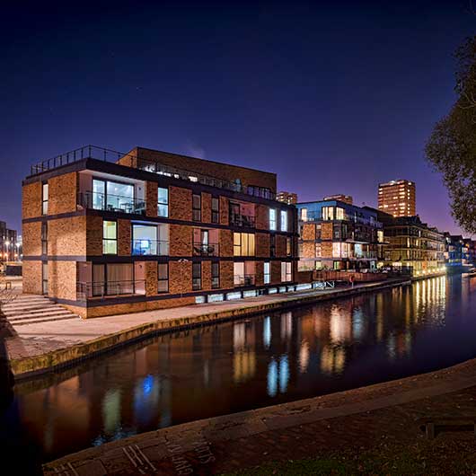 A canal side development in Hackney, east London photographed at night with lights reflecting in the water