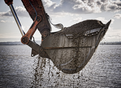 Excavator bucket lifting gravel from water