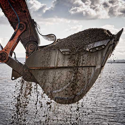 A bucket of an excavator lifting gravel from the sea in Essex