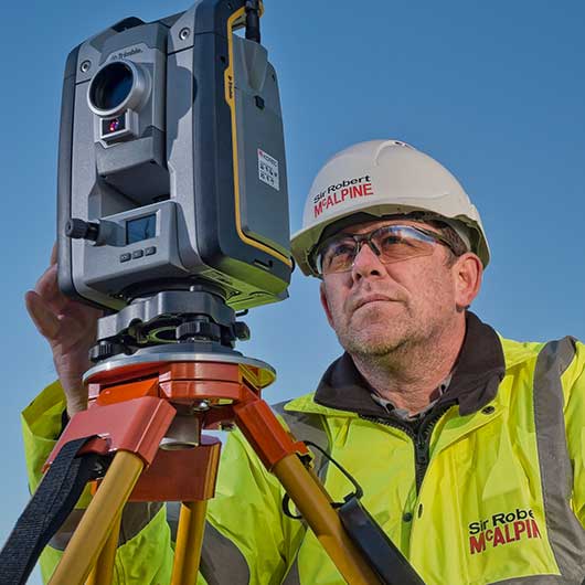 A Sir Robert MacAlpine employee using a Trimble surveying device on a construction site in West London