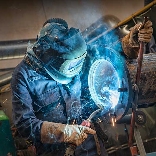 A welder working on a large steel pipe creating a blue light