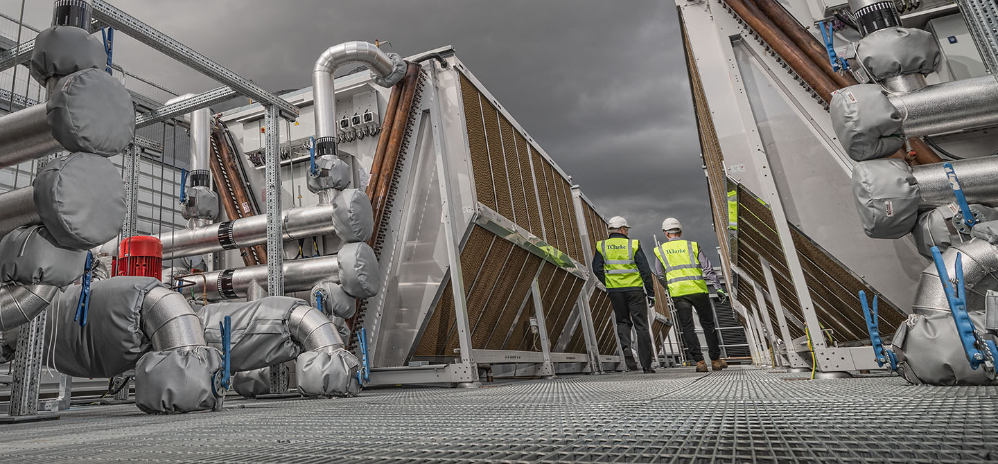 Two industrial workers in Hi-Viz inspecting chiller units on the roof of a data centre.