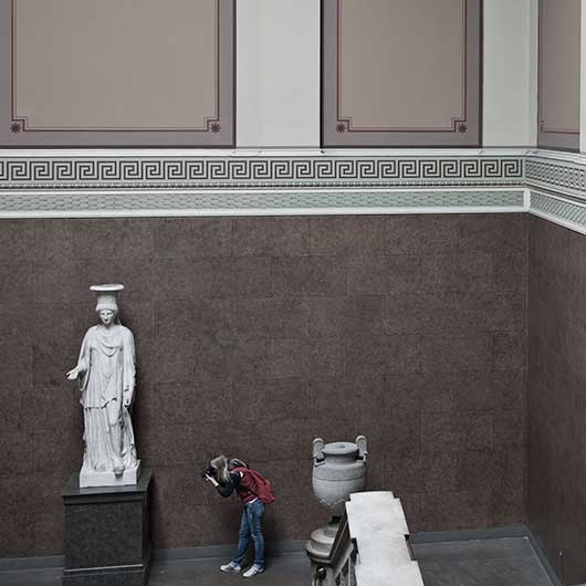 A photographer in a museum taking a picture of the bottom of a statue