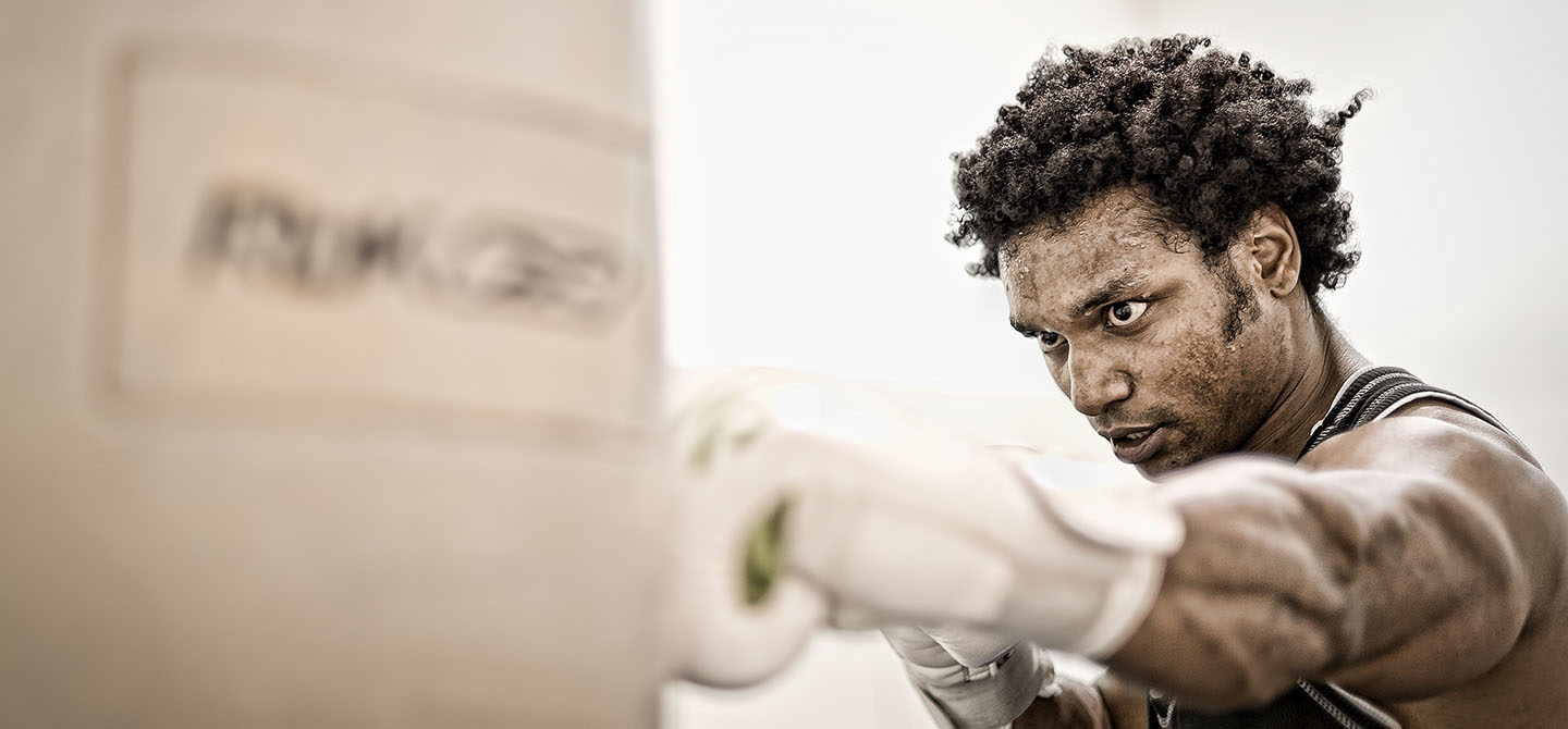 A boxer hitting a punch bag with sweat dripping from forehead