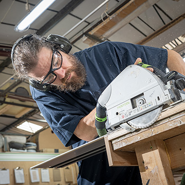 Using a circular saw in a workshop wearing ppe to comply with health and safety regulations