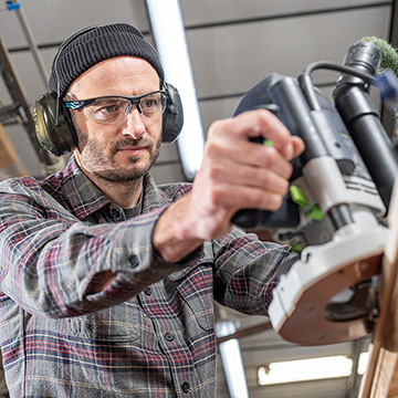 Carpenter using a router with glasses and ear defenders